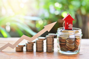 Stack of coins with arrow pointing to a jar of coins with toy house on top - Prudent financial solutions