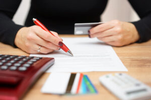 woman writing and checking credit card information - Prudent Financial Solutions