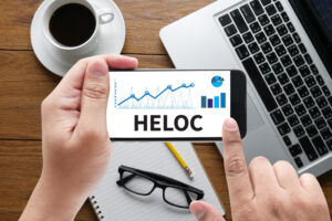 HELOC (Home Equity Line of Credit) message on hand holding to touch a phone - Prudent Financial Solutions