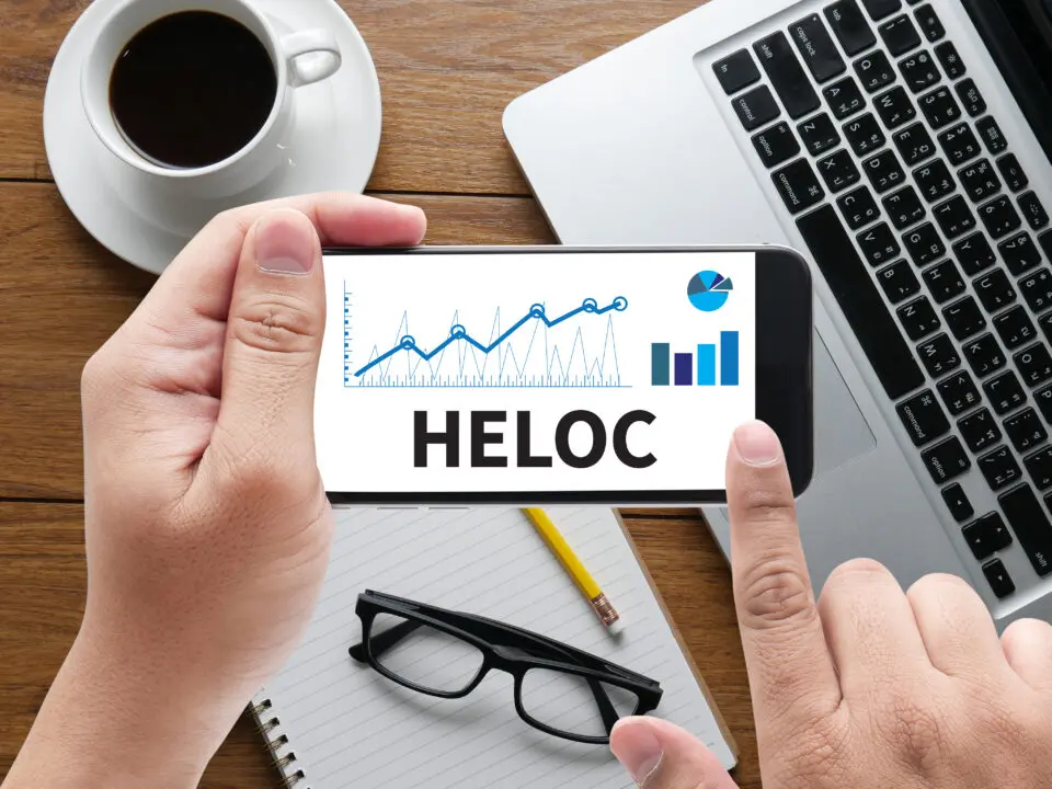 HELOC (Home Equity Line of Credit) message on hand holding to touch a phone - Prudent Financial Solutions